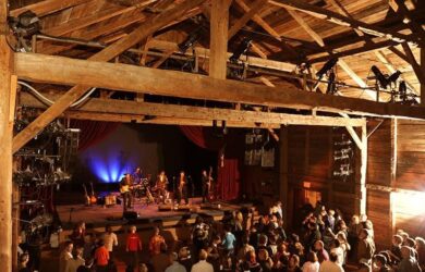Grange en bois transformée en salle de concert, avec public et scène