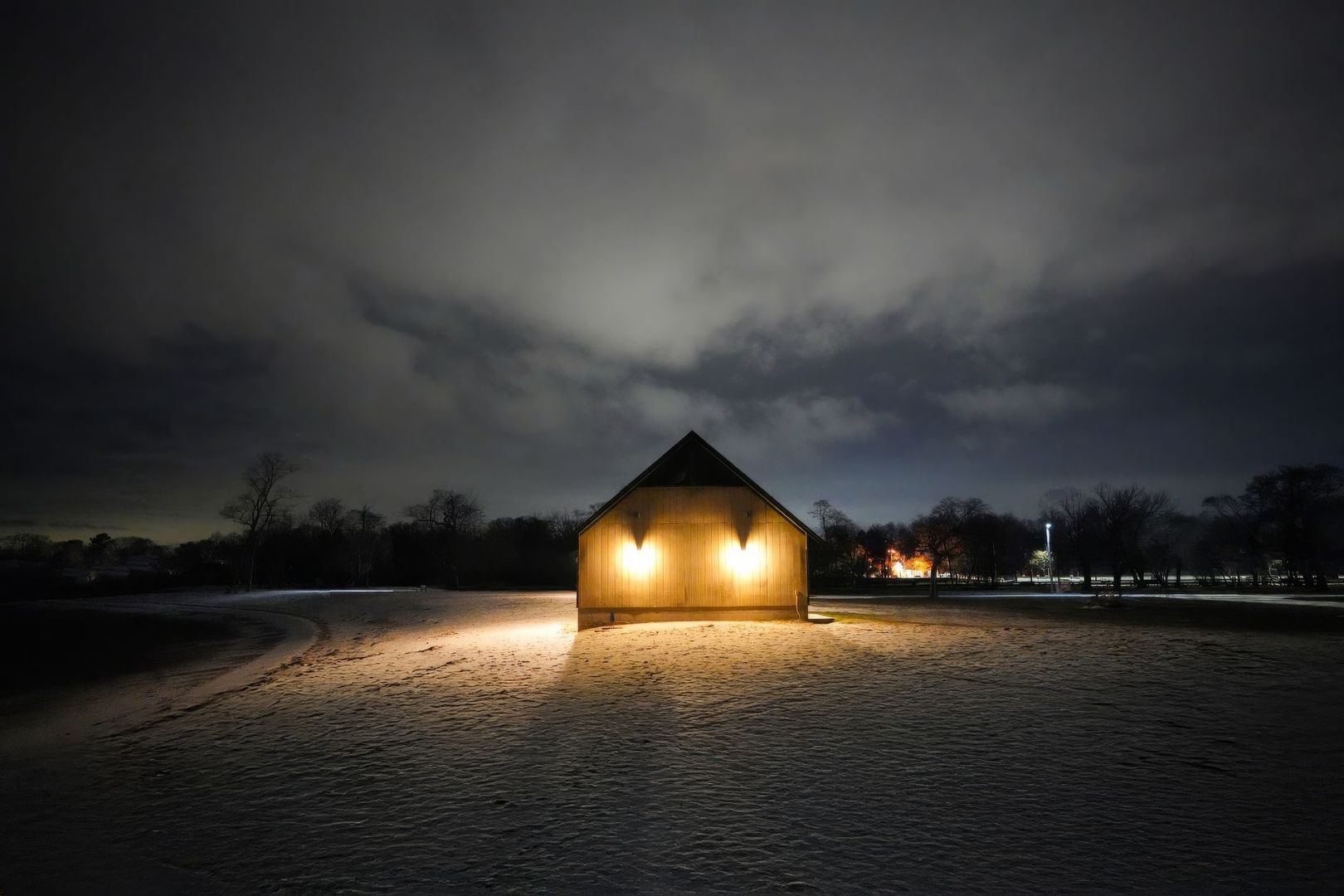 Grange en bois éclairée dans un paysage enneigé, sous un ciel sombre